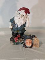 Acrylic gnome figurine with red hat and blue coat, standing on a base with mushrooms and a flower.