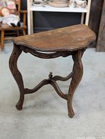 Front angle view of half moon antique wooden side table showing curved legs and intricate carved details on apron.