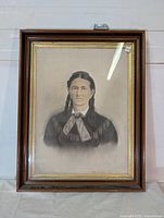 Full front view of the framed portrait showing the woman with braided hair in a monochrome drawing, the wooden frame and glass reflecting light.