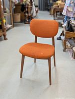 Front view of mid century modern orange upholstered chair with wooden legs showing textured fabric and some stains.
