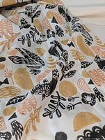 Close-up image of the scarf showing black and tan botanical and abstract block print design on white fabric.
