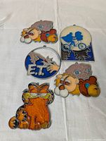 Photo of five completed stained glass crafts featuring ET and Garfield characters from the 1990s with vibrant colors and hanging loops.