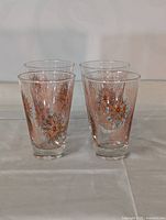 Four clear vintage glasses with orange floral and vertical line design arranged on a white cloth.