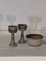 Front view of two pottery goblets and one pottery bowl on a neutral cloth background.