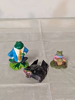 All three ceramic frog figurines shown on beige cloth background.
