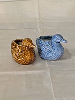 Two ceramic bird planters side by side on a cloth surface, showing front and side views.