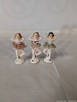 Three antique ceramic dancing ballerina figurines standing side by side on a flat surface, showing overall height and details.