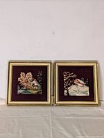Front view of two framed needlepoint art pieces depicting a house in different seasonal scenes, showing their overall size and condition.