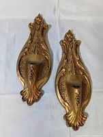 Top-down view of matching gold tone wall sconces with ornate detailing and single candlestick holdres
