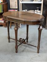 Full view of wooden side table with octagonal top, carved edge, turned legs, and decorative cross stretchers, placed on a gray carpet with some water damage visible on the wood surface.