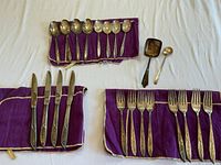 Overall view showing spoons, knives, forks on purple cloth and two serving pieces