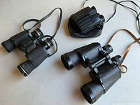 Three binoculars displayed on flat surface: Sunscope President 7x50, Empire Model 218, Discoverer 10x28 with straps and pouch visible