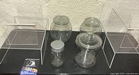 Full view of six acrylic stands and four glass canisters on a black surface showing size and shape differences