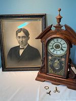 Clock and framed portrait together on table with clock winding keys visible