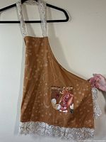 Full view of one brown apron with lace straps and bottom lace trim, pocket with vintage floral print.