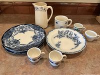 Full set of items on countertop including 3 J.H.W & Sons plates, shallow bowl by Societe Ceramique, tall pitcher, and 5 small cups and mugs