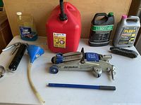 Overall view of the lot including the gas can, fluids, jack, funnel, grease gun, and brushes on a white table