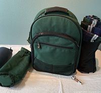 Closed view of dark green backpack with rolled-up plaid blanket and green pouch
