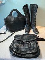 Two black leather bags and one pair of tall black leather boots on a white surface against a blue wall.