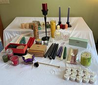 Wide view of all candles, holders, candle snuffer, and accessories displayed on white cloth surface