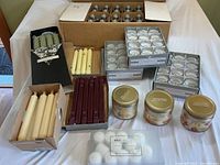 Full overview of all candles and oil lamp cartridges arranged on table, including votive candles, various taper candles, scented jars and oil cartridges