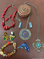Full lot overview showing colorful ethnic jewelry pieces including red beaded necklace, decorative box, silver chain necklaces with ethnic pendants, dolphin pendant, and multi-colored earrings.