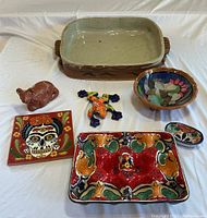 All six pottery items displayed on white cloth including dishes, frog figurine, tile trivet, and bowl.