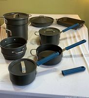 Full view of entire cookware set arranged on white cloth, showing pots, pans, lids, steamer baskets, silicone covers and baking pan.