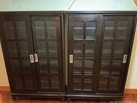 Photo showing two narrow dark wood cabinets side by side with sliding doors featuring ribbed glass panels and metal handles.