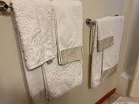 Two cream-colored bathroom towels hanging on towel racks showing floral embossed and ribbed pattern with beige textured trim detail.