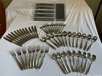 Full set of flatware arranged on a white cloth showing knives, forks, spoons, butter spreaders, and organizer tray