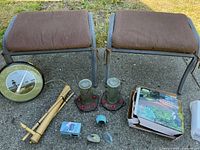 Photo showing two brown cushioned benches, a round garden thermometer, bamboo stakes, two glass hummingbird feeders with red feeding ports, and a boxed garden solar spotlight and bird feeders, all laid out on concrete ground.