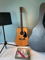 Full view of guitar standing next to case and music stand with sheet music on table