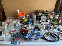 Top down image of various home repair supplies showing tapes, hand cleaner, hooks, bungee cords, WD-40, and other hardware.