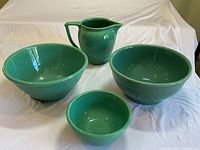 Four jade green stoneware pieces displayed together: three bowls of varying sizes and a pitcher.