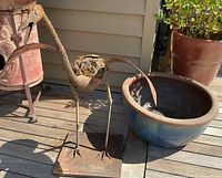 Blue ceramic planter and metal heron yard art on wooden deck; planter is round and blue glazed, heron is rusted metal