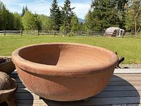 Front and top angle view of large terracotta basin planter outdoors on wooden deck with grassy background.