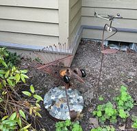 Front view of bird and balancing frog metal sculptures outdoors next to house corner