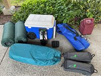 Photo showing cooler, air mats, tent bag, camp shovel box, fuel container, and lantern pouch arranged on a concrete floor