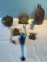 Collection of unique decor items displayed on white surface including clock, apple weight, horse head, glass candle holder, and small ornaments.