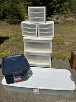 Photo showing all plastic storage items stacked outside on concrete and grass background, including large and small drawer units and totes.