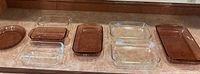 Eight Pyrex baking dishes on counter including four rose-colored and four clear glass dishes of various sizes and shapes for casseroles, bread, and pie.
