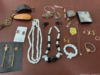 Overview of assorted costume jewelry and accessories laid out on a table, showing necklaces, bracelets, earrings, wristwatch, and decorative bookmarks.