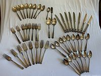 Full set of Roger’s Bros silver plated flatware arranged and visible showing knives, forks, spoons, and teaspoons, all with Victorian floral handles and tarnish.