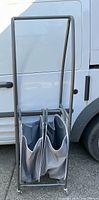 Full view of the gray metal rolling laundry rack with two cloth bins visible attached inside.