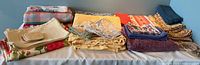 Eight large tablecloths folded on table, variety of colors and patterns visible