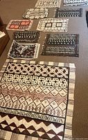 Assorted Tapa bark cloth placemats laid on carpet with various geometric and natural motifs in white, brown, and black with some red accents.
