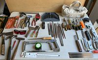 Image showing a wide assortment of hand tools on a white table, including pliers, files, screwdrivers, wrenches, and a white canvas tool bag.
