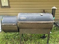 Full view of the pellet grill showing main cooking chamber and pellet hopper on side, with rust and weathering on surface.