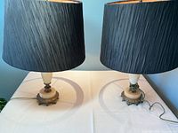 Two table lamps with round cream marble bases and black pleated fabric shades on a white table.